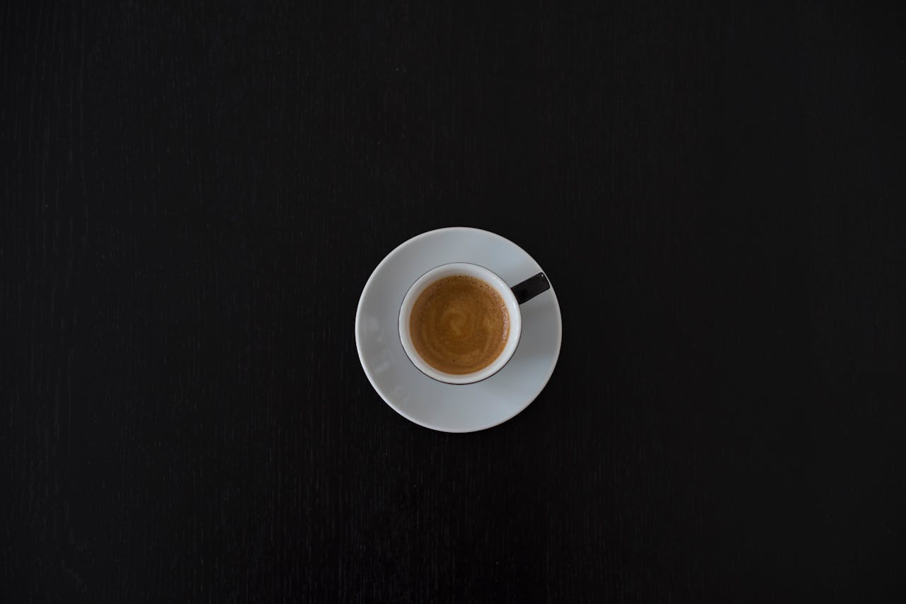 about-us Flat lay of a white coffee cup with espresso on a black table, highlighting minimalist design.