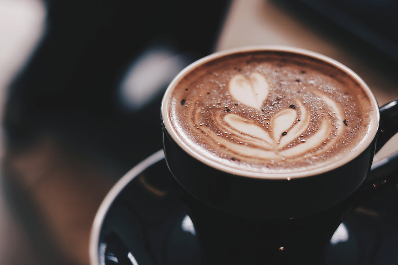 heros-img Warm mocha with heart-shaped latte art in a black ceramic cup on a saucer.